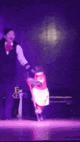 a woman stands on a stage with a purple light behind her
