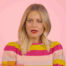 a woman wearing a pink and yellow striped sweater with the word good housekeeping on the bottom