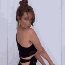 a woman in a black top is standing in front of a white wall looking over her shoulder .
