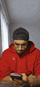 a man wearing a red hoodie and a black hat is looking at his phone