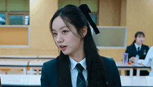 a young woman in a school uniform and tie is sitting at a table in a cafeteria .