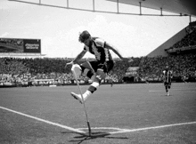 a black and white photo of a soccer player jumping in the air with a sign behind him that says deportes da sorte