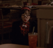 a girl wearing glasses and a bow tie sits at a table with a drink in front of her
