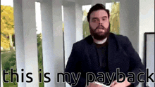 a man with a beard is standing in front of a sign that says " this is my payback "