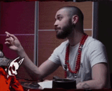a man with a beard wearing a white shirt and a red necklace
