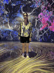 a woman stands in front of a wall with a painting of flowers on it