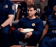 a man in a firefighter uniform is sitting on a couch eating popcorn .