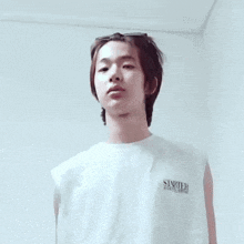 a young man wearing a white tank top and sunglasses is standing in front of a white wall .