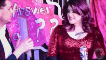 a woman in a red sequined dress is standing next to a man holding a sign that says answer