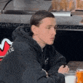 a man in a black hoodie sits at a table holding a glass of beer