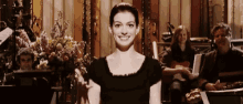 a woman in a black dress is smiling in front of a group of people