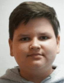 a young boy with short hair is wearing a grey sweatshirt