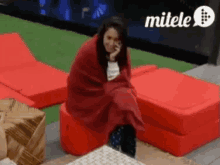 a woman is wrapped in a red blanket while sitting on a red chair ..
