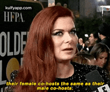 a woman with red hair is talking into a microphone in front of a crowd .