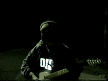 a man is playing a guitar in the dark and his shirt says autotune