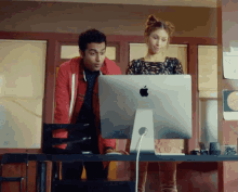 a man and a woman are looking at an apple computer monitor