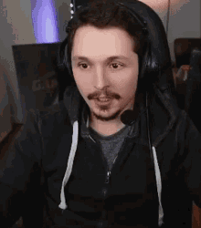 a man with a beard is wearing headphones and a microphone while sitting in a gaming chair .