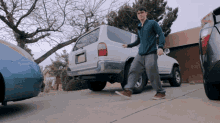 a man in a blue jacket is walking towards a white suv with a license plate that says new mexico