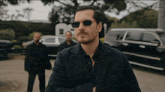a man wearing sunglasses stands in front of a car