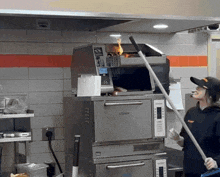 a person holding a mop in front of a stainless steel oven with a fire coming out of the top