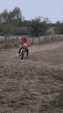 a man in a red shirt is riding a motorcycle on a dirt road
