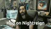 a man with long hair and a beard sits in front of a microphone with the words hop on nightreign written below him