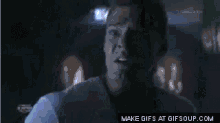 a man in a blue shirt is making a funny face while sitting in a car at night .