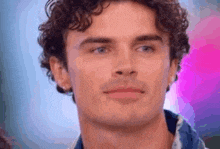 a close up of a man 's face with curly hair and blue eyes looking at the camera .