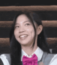 the girl is wearing a school uniform and a pink bow tie and smiling .