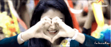 a woman making a heart shape with her hands in front of her eyes