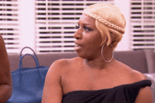 a woman wearing a braided headband and hoop earrings is sitting in front of a window