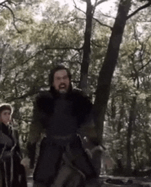 a man with a beard is standing in the woods .