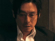 a man wearing glasses and a suit looks down at something