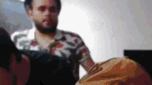 a man with a beard and a floral shirt is standing in a room with other people .
