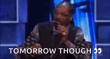 snoop dogg is sitting in front of a microphone with the words tomorrow though behind him .