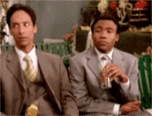 two men in suits sitting next to each other drinking