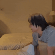 a man in a blue shirt is sitting on a bed with white sheets