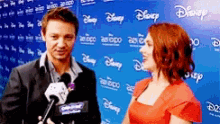 a man and a woman are talking in front of a disney expo wall