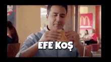 a man in a blue shirt is eating a hamburger with the words efe kos written above him