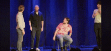 a group of men are standing on a stage and one of them is sitting in a chair and saying `` i hate you '' .