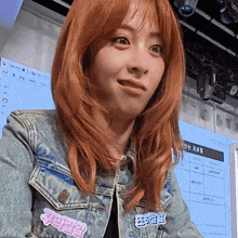 a woman with red hair wearing a denim jacket has a sticker on her jacket that says ' korean '