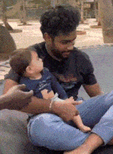 a man is sitting on a couch holding a baby in his lap .