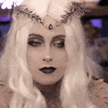 a woman with long white hair and a crown on her head is wearing black lipstick .