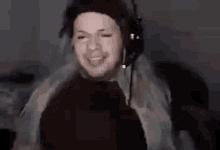a man wearing a hat and headphones is smiling while sitting in front of a computer screen .