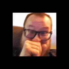 a man wearing glasses is covering his mouth with his hand .