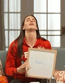a woman in a red hoodie is sitting on a couch holding a whiteboard .