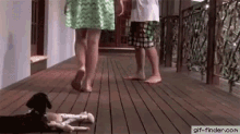 a woman and a man are walking down a wooden walkway while a dog lays on the floor .