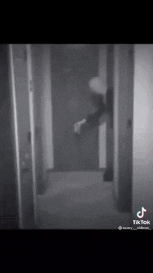 a black and white photo of a person standing in a hallway holding a gun .