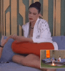a woman in a white jacket and red pants sits on a couch