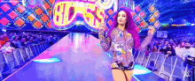 a woman with purple hair is walking down a runway in front of a crowd at a wrestling event .